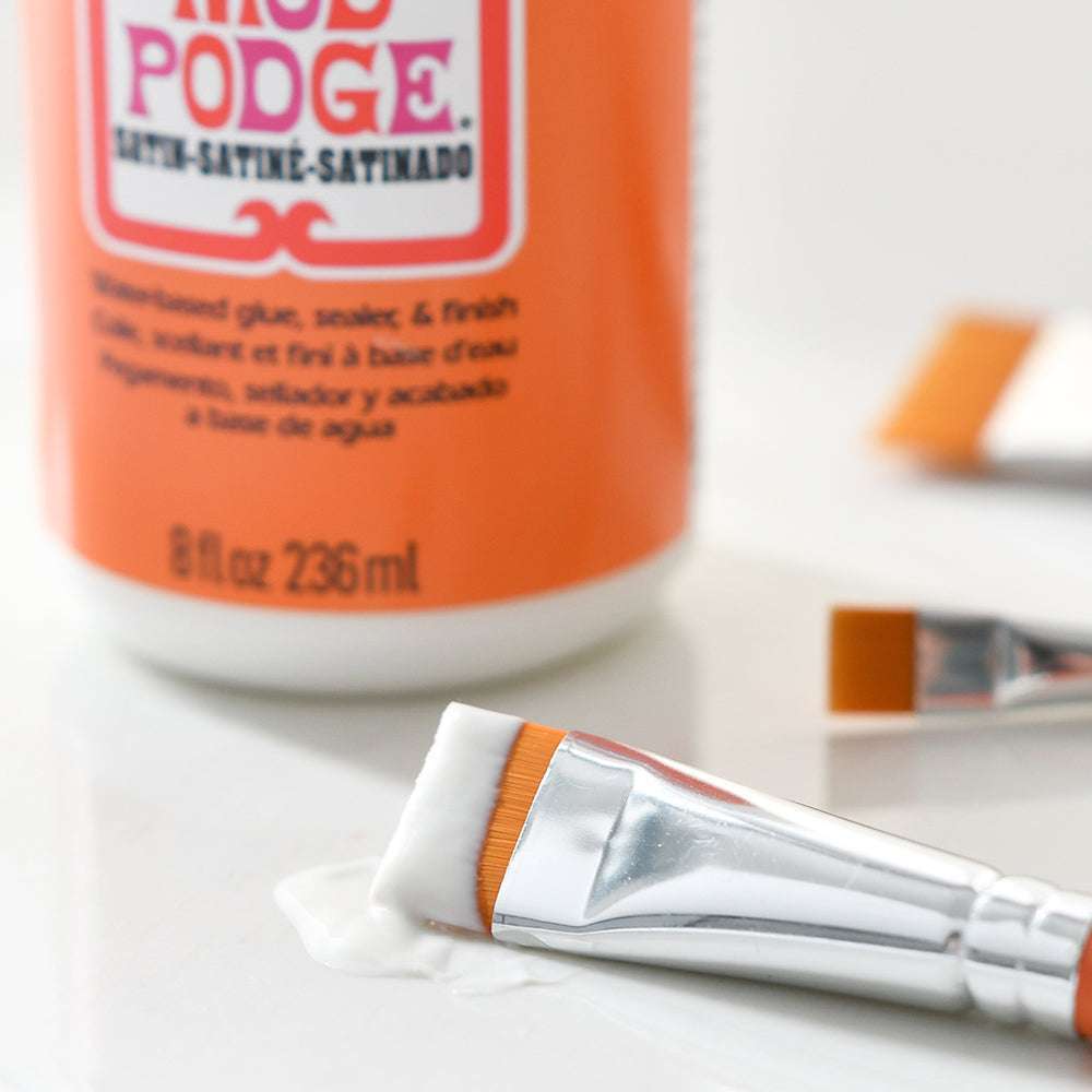 Nahaufnahme eines Plaid Enterprises Pinsel-Sets mit hochwertigen synthetischen Borsten, das einen Pinsel mit Weißleim neben einer Mod Podge-Flasche zeigt - ideal für all Ihre Bastelarbeiten.