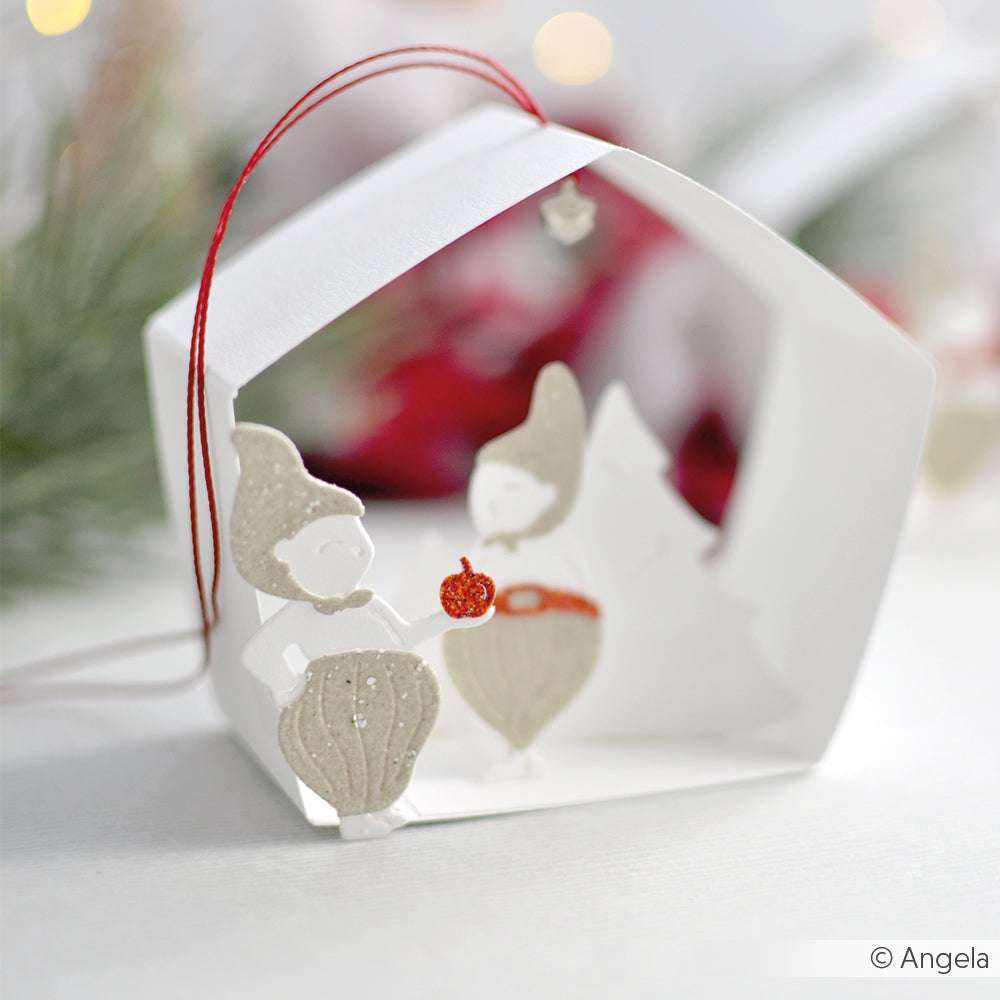 Papierornament mit zwei Zwergen im Inneren, von denen einer ein rotes Ornament in der Hand hält. Gestaltet mit Alexandra Renke Motivstanze Wichtel Alvar Dies, vor einem weichen weihnachtlichen Hintergrund.