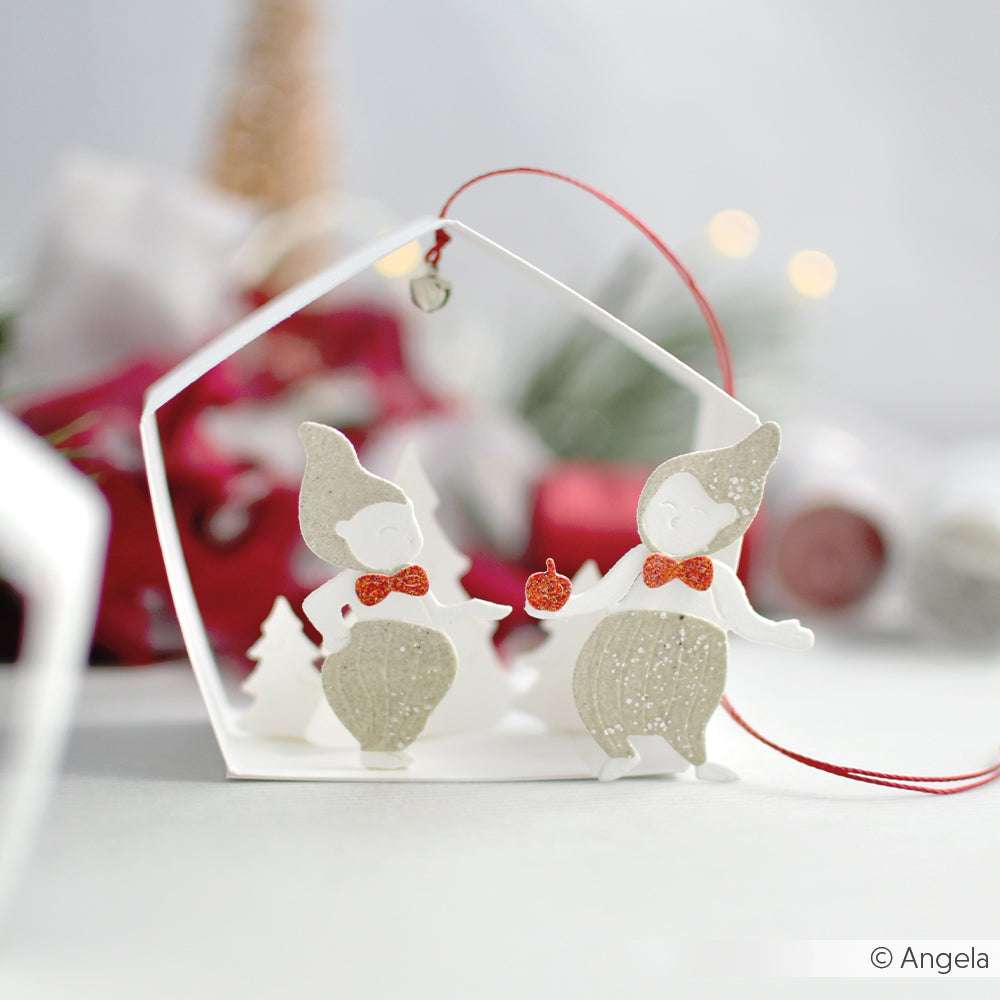 Zwei Elfenornamente aus Papier mit roten Schleifen und Hüten, die mit WOW Embossing Powder hergestellt wurden, stehen in einem weißen Rahmen mit festlichem Dekor im Hintergrund.