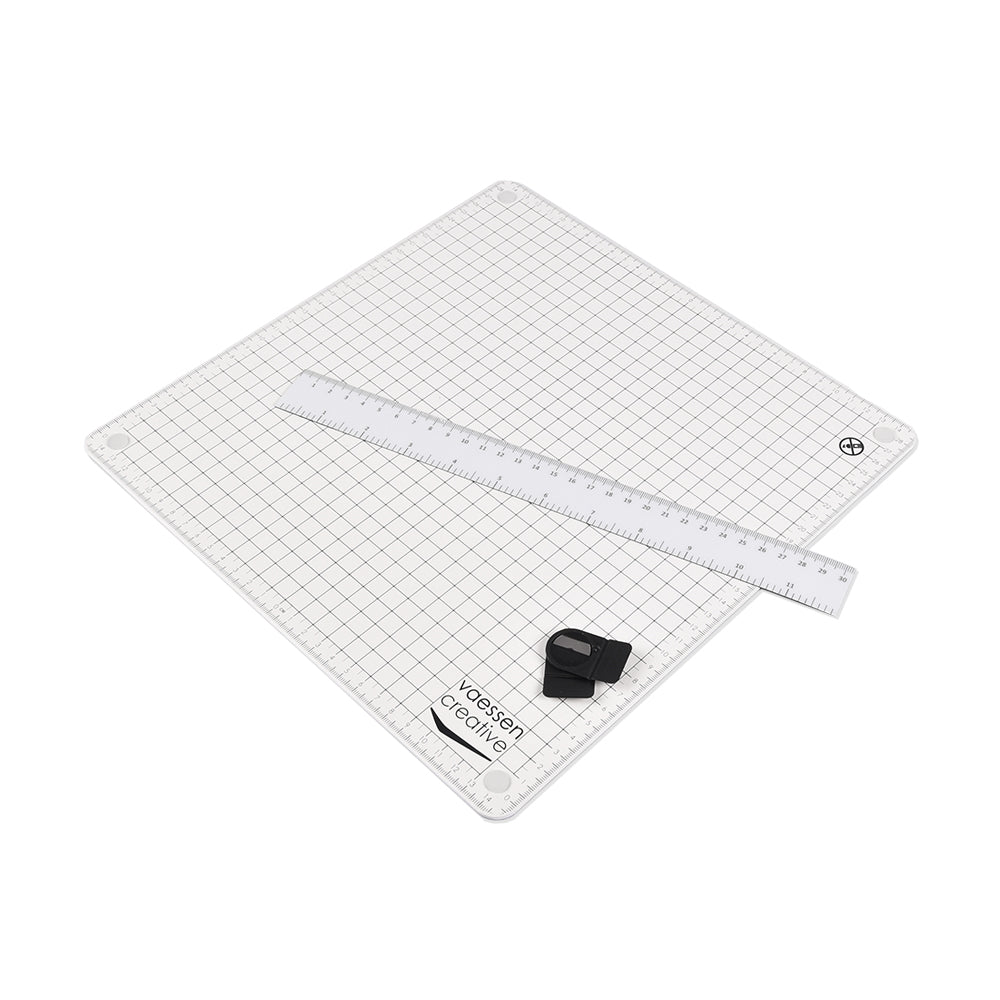 Eine selbstheilende Vaessen Schneidematte mit Raster, auf der ein weißes Lineal und zwei schwarze Klingenhalter liegen - ideal zum Basteln.