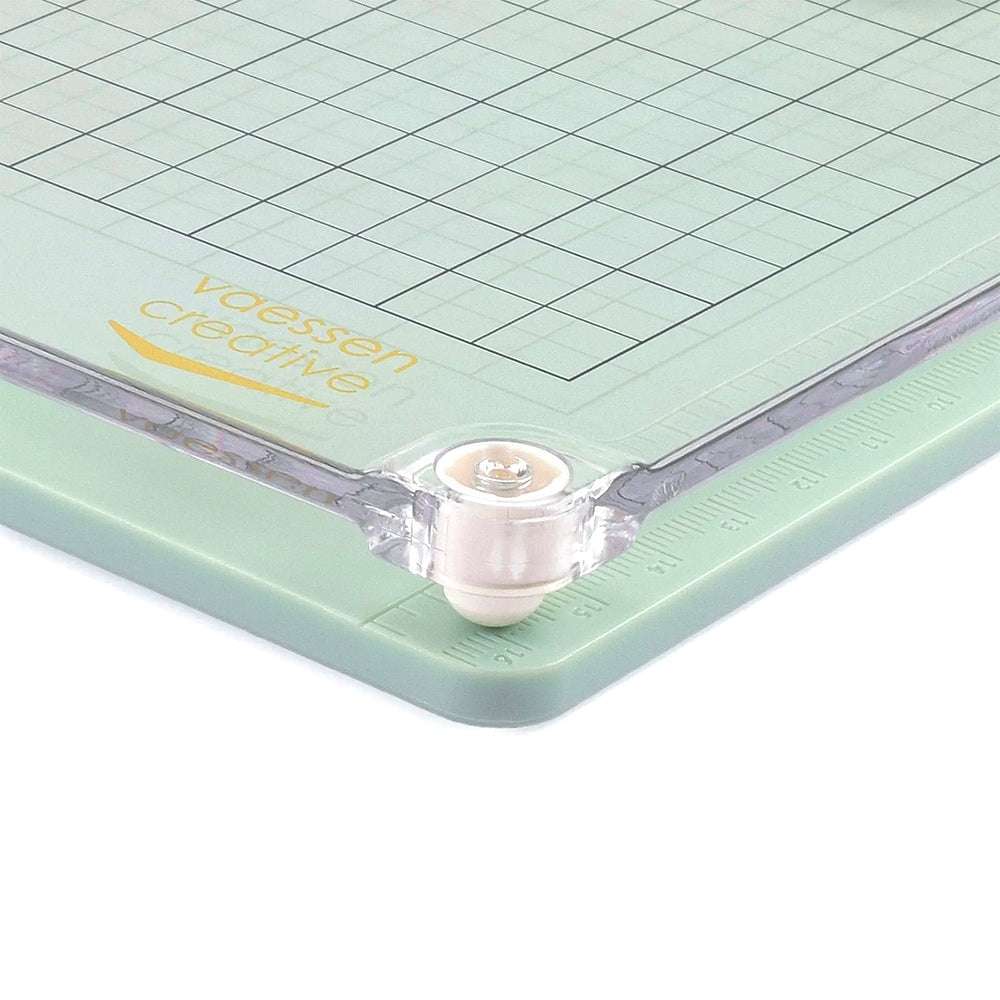 Nahaufnahme einer grünen Vaessen Crafting-Schneidematte mit Rasterlinien und abgerundeten Ecken, die mit einem weißen Rollrad ausgestattet ist - eine ideale Oberfläche für Ihr Stempelwerkzeug oder Stamp Easy beim Arbeiten mit Klarsichtstempeln.