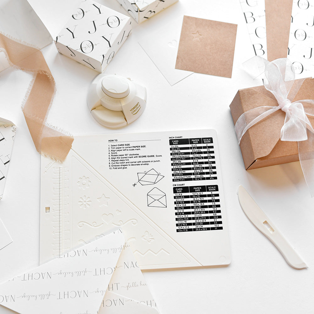 Vaessen Geschenkverpackungsmaterialien, ein Falzbrett-Karten-Maker, und eingepackte Geschenke mit Bändern und Papier auf Weiß - ideal für kreative Geschenkverpackungen basteln oder Umschläge mit Stil falten.