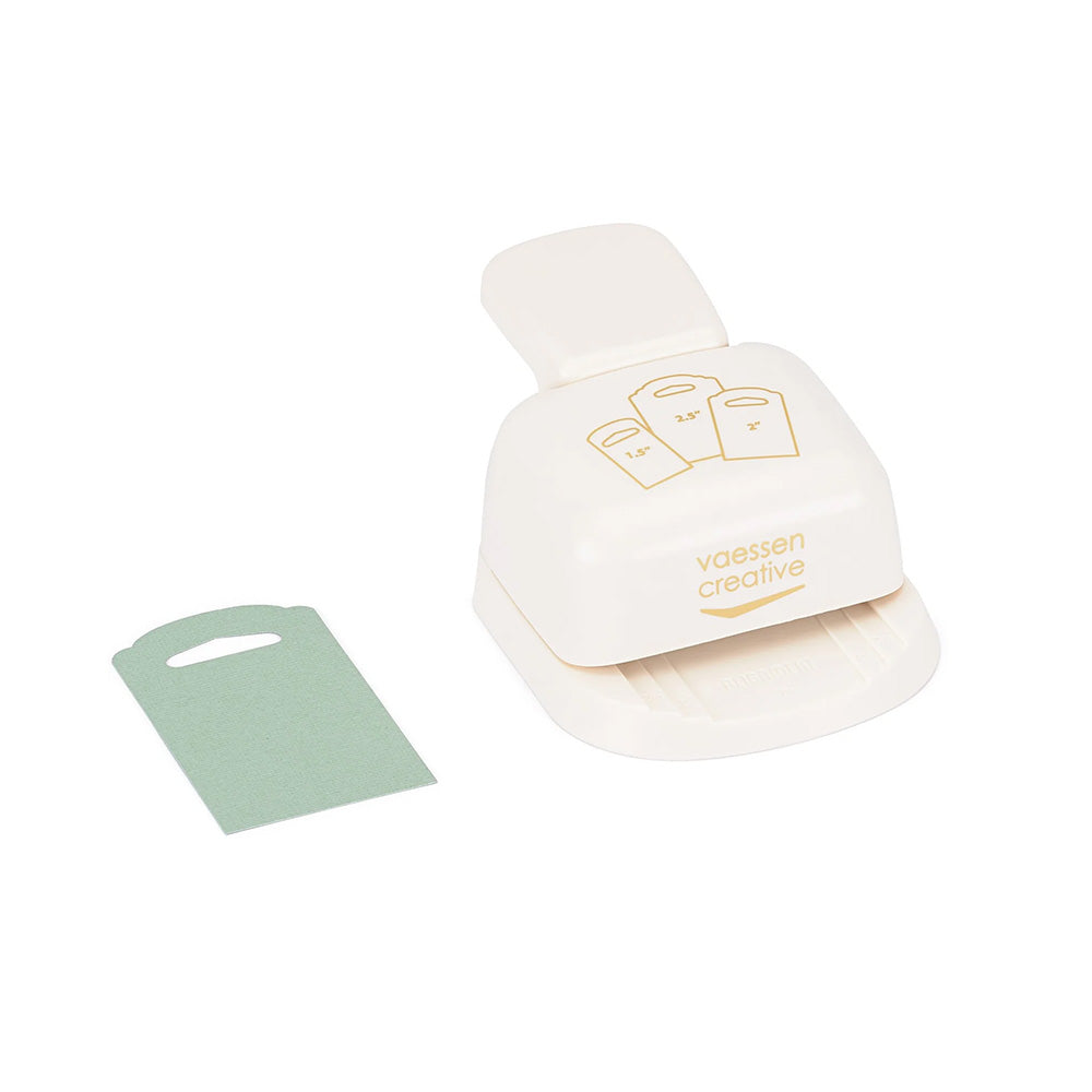Ein weißer 3-in-1-Papierstanzer „Vaessen Stanzer“ zum Herstellen von Anhängern, daneben auf weißem Hintergrund ein grüner, ausgestanzter Anhänger – ein unverzichtbares Bastelwerkzeug, ideal zum Stanzen von Etiketten.