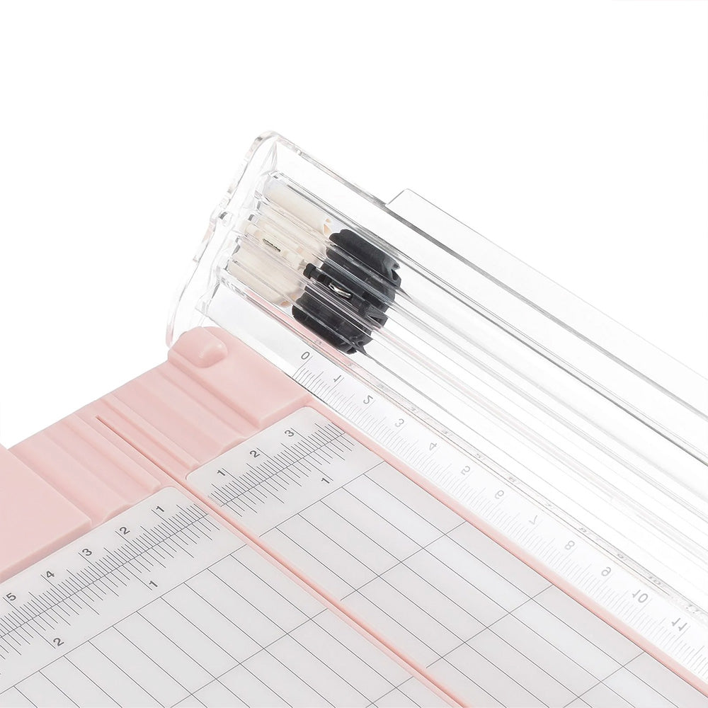 Drei Stifte in einem durchsichtigen Halter ruhen auf einem rosafarbenen Vaessen-Papierschneider mit Linealen und Messrastern, perfekt für Scrapbooking.