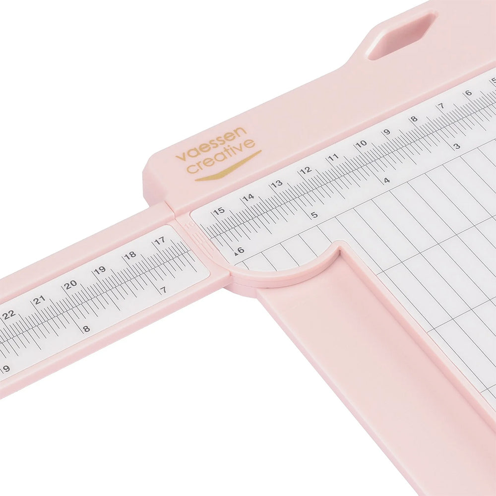 Nahaufnahme eines rosafarbenen Vaessen-Papierschneiders mit Lineal, Rasterlinien und Ritzwerkzeug für präzises Messen, Schneiden und einfaches Ritzen.