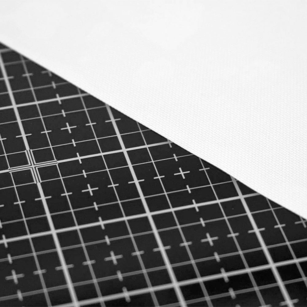 Eine schwarze Tonic Studios-Schneidematte mit weißen Gitternetzlinien, auf der ein weißes Blatt Leinwand liegt.